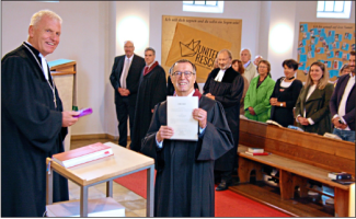 Stolz zeigt er seine Ernennungsurkunde zum Prädikanten: Dr. Florian Garnich (Mitte) hat das Dokument soeben aus den Händen von Dekan Peter Bertram (links) entgegengenommen.